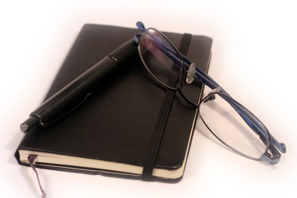 A diary, pen and reading glasses on a desk